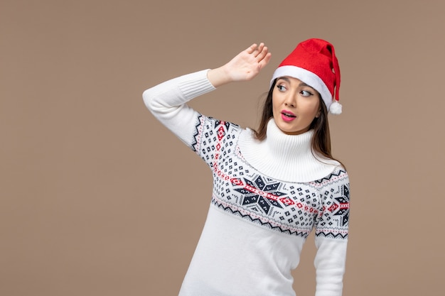茶色の背景のクリスマスの休日の感情に赤いクリスマスキャップと正面図若い女性