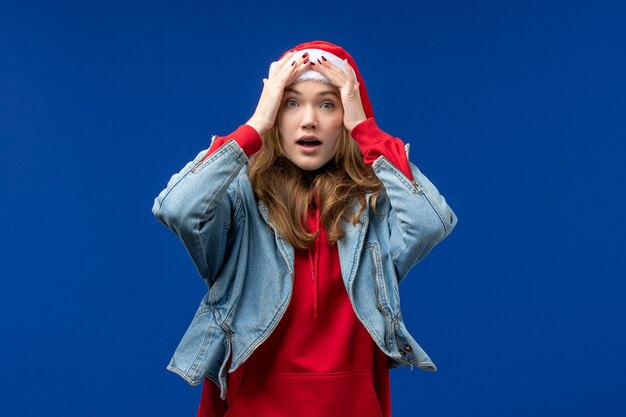 Вид спереди молодая женщина с красной рождественской шапкой на голубом фоне цвета рождественских эмоций