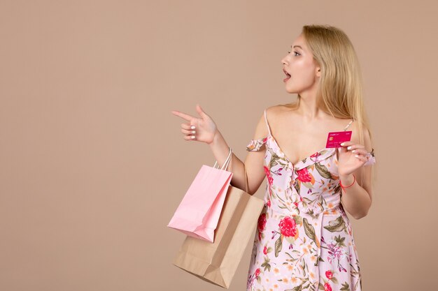 茶色の壁に買い物袋と銀行カードを持つ若い女性の正面図