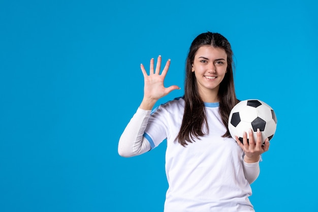Вид спереди молодая женщина с футбольным мячом на синей стене