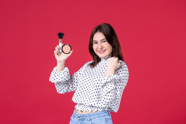 Front view of young female with tassel and powder for make-up on red wall