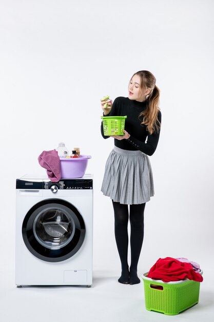 Front view of young female with washer and dirty clothes on the white wall