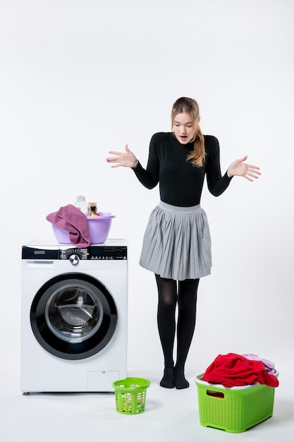 Front view of young female with washer and dirty clothes on white wall