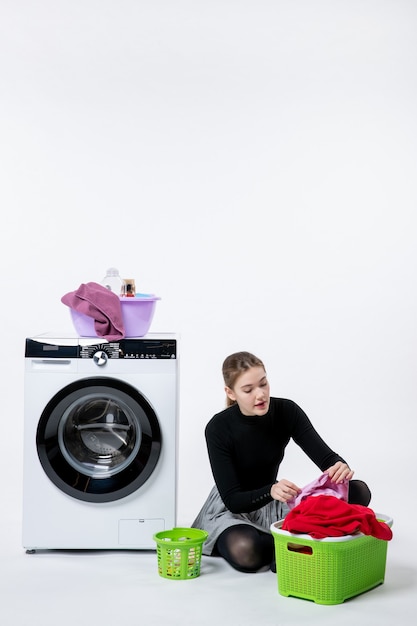 Вид спереди молодая женщина со стиральной машиной и грязной одеждой на белой стене