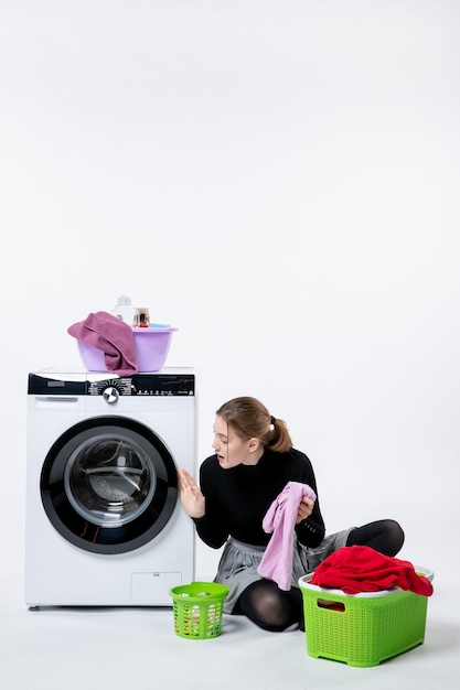 Front view of young female with washing machine folding dirty clothes on a white wall