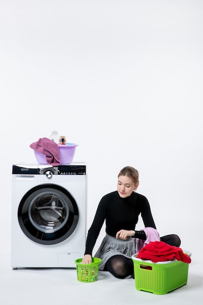 Front view of young female with washing machine folding dirty clothes on white wall