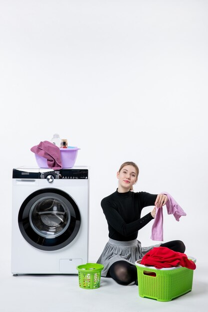 Front view of young female with washing machine folding dirty clothes on white wall