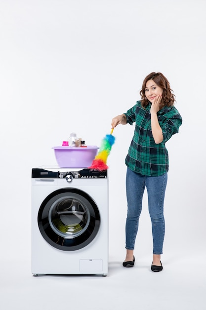 Front view of young female with washing machine holding dust cleaner on the white wall