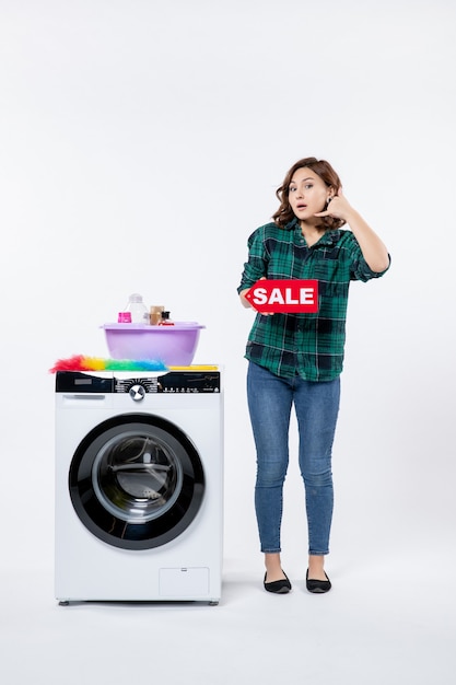 Front view of young female with washing machine holding sale banner on white wall