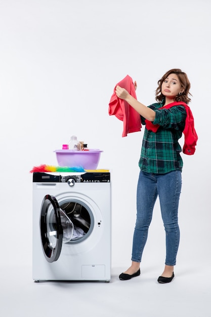 Free photo front view of young female with washing machine preparing clothes for wash on light wall