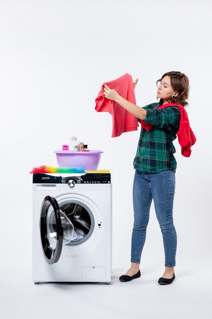白い壁に洗濯物を洗うために洗濯機を準備している若い女性の正面図