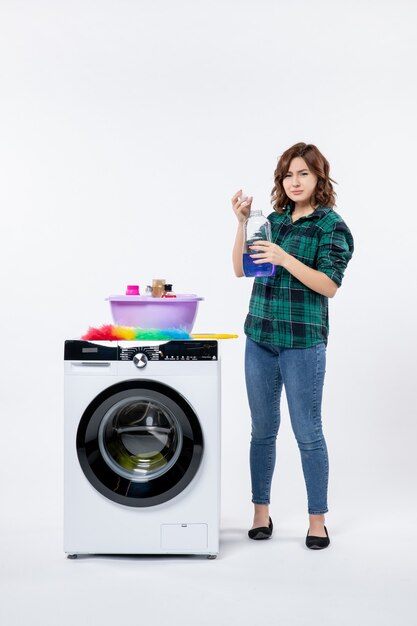 Front view of young female with washing machine preparing liquid powder on the white wall