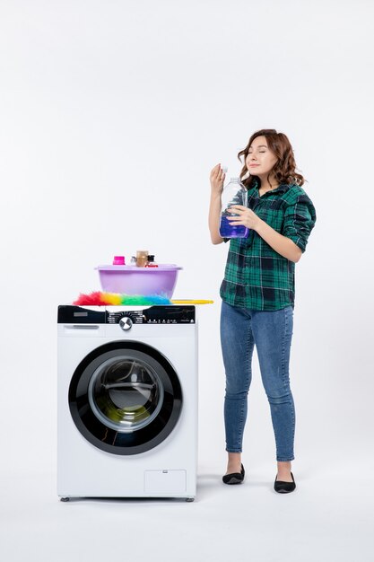 Front view of young female with washing machine preparing liquid powder on white wall