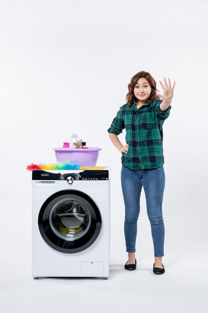 Front view of young female with washing machine on white wall