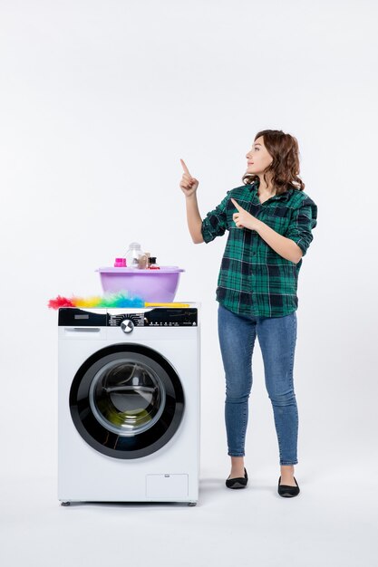 Front view of young female with washing machine on white wall