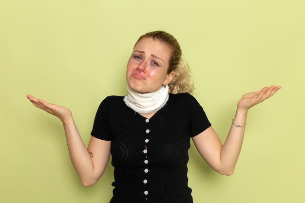 Foto gratuita giovane femmina di vista frontale con l'asciugamano bianco intorno alla sua gola che si sente molto malato e malato che posa sulla salute di colore femminile di malattia di malattia della parete verde