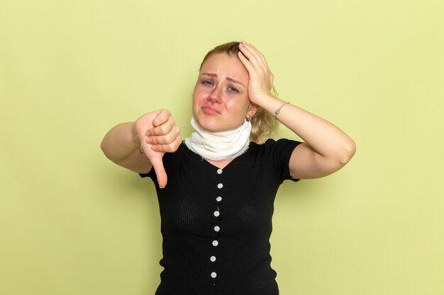 Front view young female with white towel around her throat feeling very sick and ill showing unlike sign on green wall illness sickness female color health