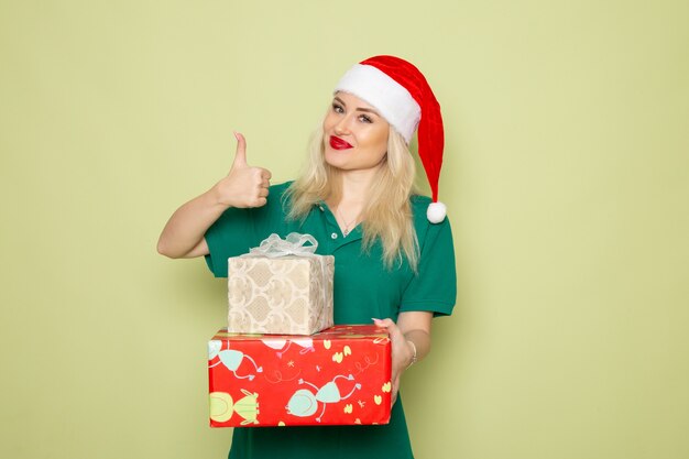 Vista frontale della giovane donna con regali di natale sulla parete verde