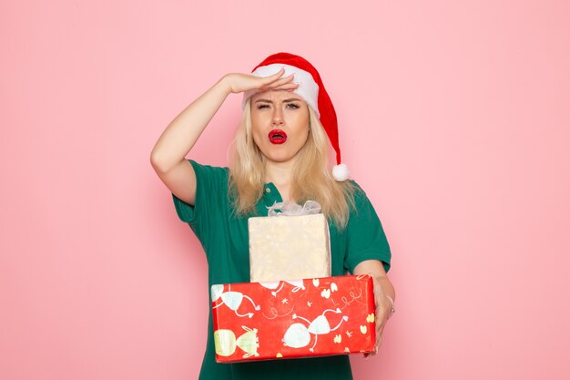 Вид спереди молодой женщины с рождественскими подарками на розовой стене