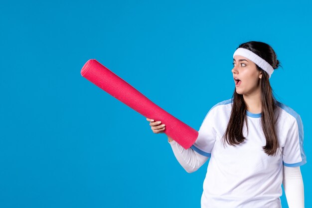 Front view young female with yoga mat on blue wall