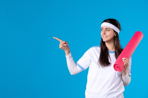 Front view young female with yoga mat on blue wall