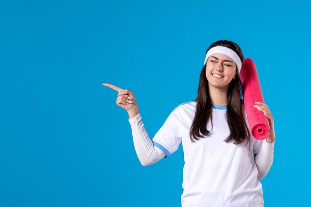 Front view young female with yoga mat on blue wall