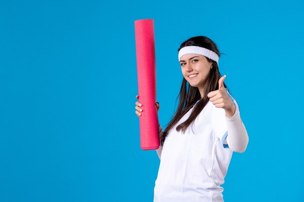 Front view young female with yoga mat on blue wall