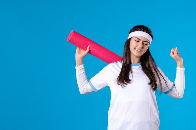 Vista frontale giovane femmina con materassino yoga sulla parete blu