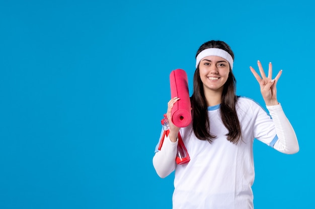 Front view young female with yoga mat on blue wall