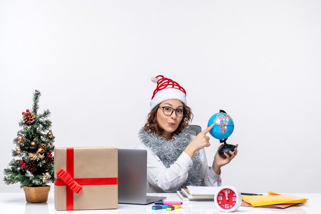 Front view young female worker sitting before her place holding earth globe on a white background
