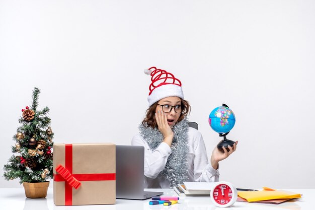 Front view young female worker sitting before her place holding earth globe on the white background