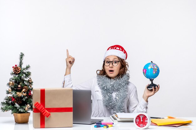 Front view young female worker sitting before her place holding earth globe on the white background