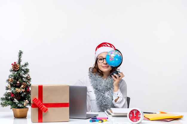 Front view young female worker sitting before her place holding earth globe on the white background