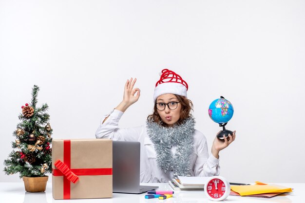 Front view young female worker sitting before her place holding earth globe on white background