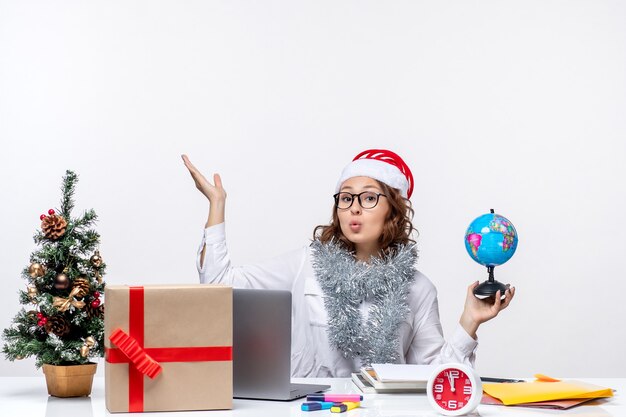 Front view young female worker sitting before her place holding earth globe on white background