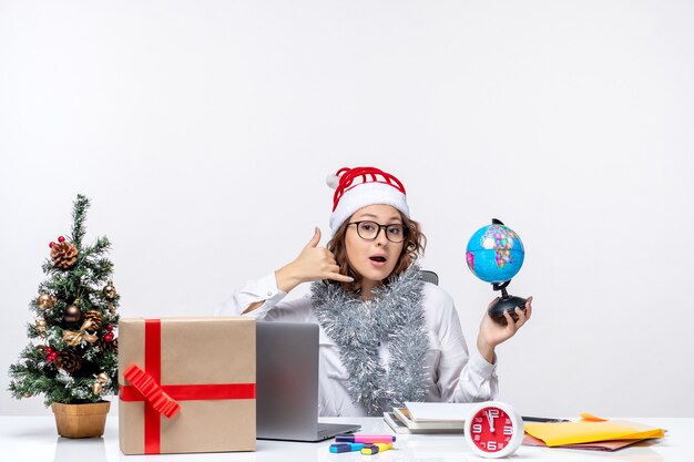 Front view young female worker sitting before her place holding earth globe on white background