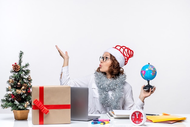 Front view young female worker sitting before her place holding earth globe on white background