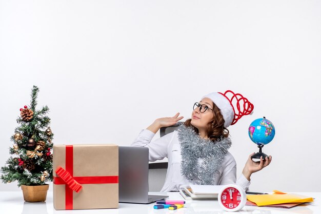 Front view young female worker sitting before her place holding earth globe on white background