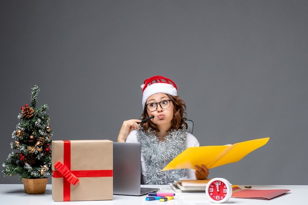 Free photo front view young female worker sitting before her place and working with documents on grey background