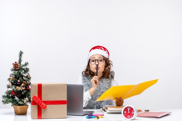 Front view young female worker sitting before her place and working with documents on a white background