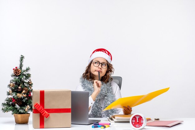 Front view young female worker sitting before her place and working with documents on white background