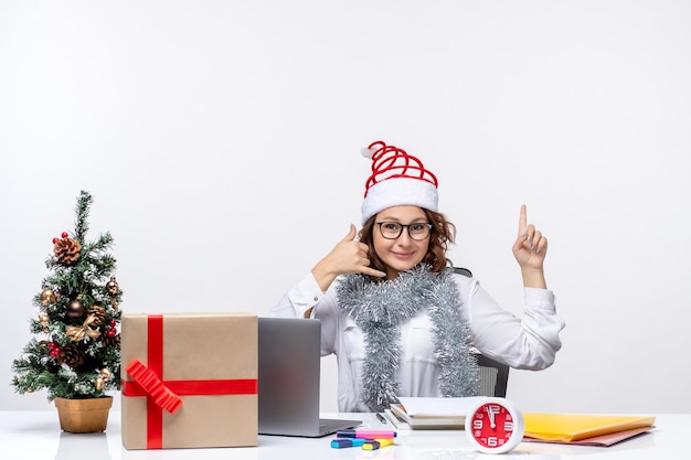 Front view young female worker sitting before her working place smiling on white background