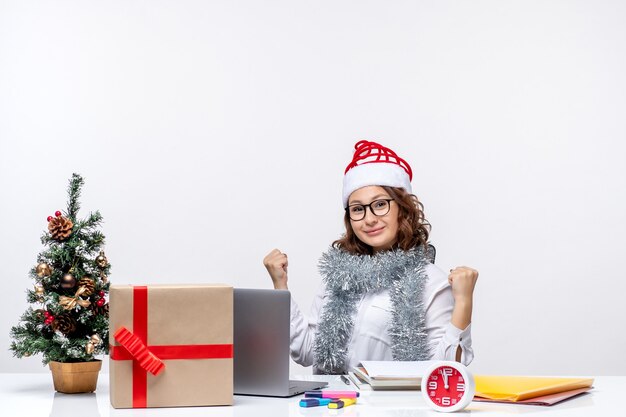 Front view young female worker sitting before her working place on a white background