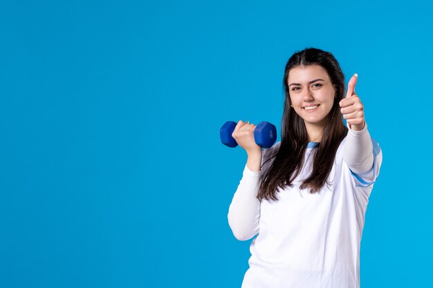 青い壁に青いダンベルで運動している正面図若い女性