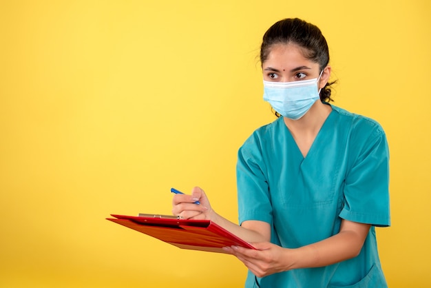 Front view of young female writing something on a clipboard on yellow wall