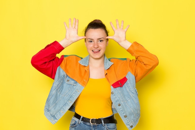 A front view young female in yellow shirt colorful jacket and blue jeans funny posing