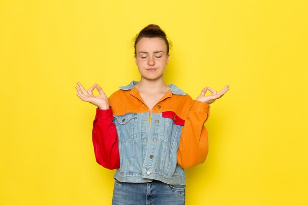 黄色いシャツのカラフルなジャケットとブルージーンズの瞑想で正面の若い女性