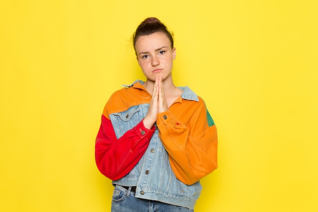 A front view young female in yellow shirt colorful jacket and blue jeans posing and praying