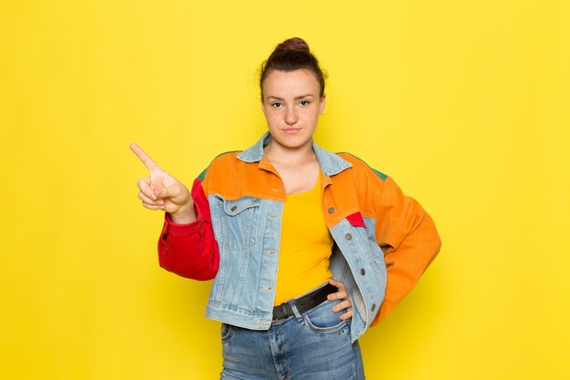 A front view young female in yellow shirt colorful jacket and blue jeans posing