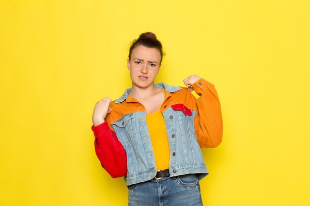 A front view young female in yellow shirt colorful jacket and blue jeans posing